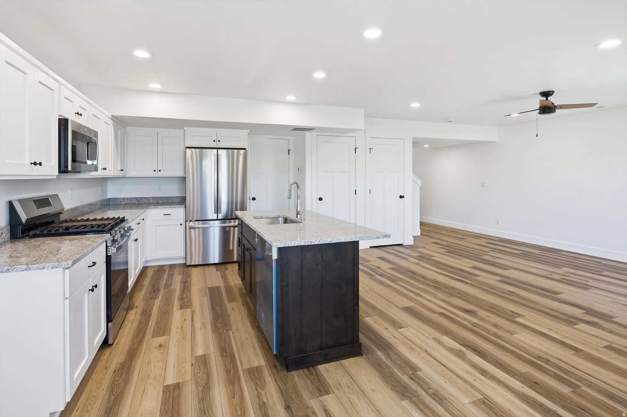 Open-concept kitchen featuring white cabinetry, stainless steel appliances, and a granite-topped island with an undermount sink