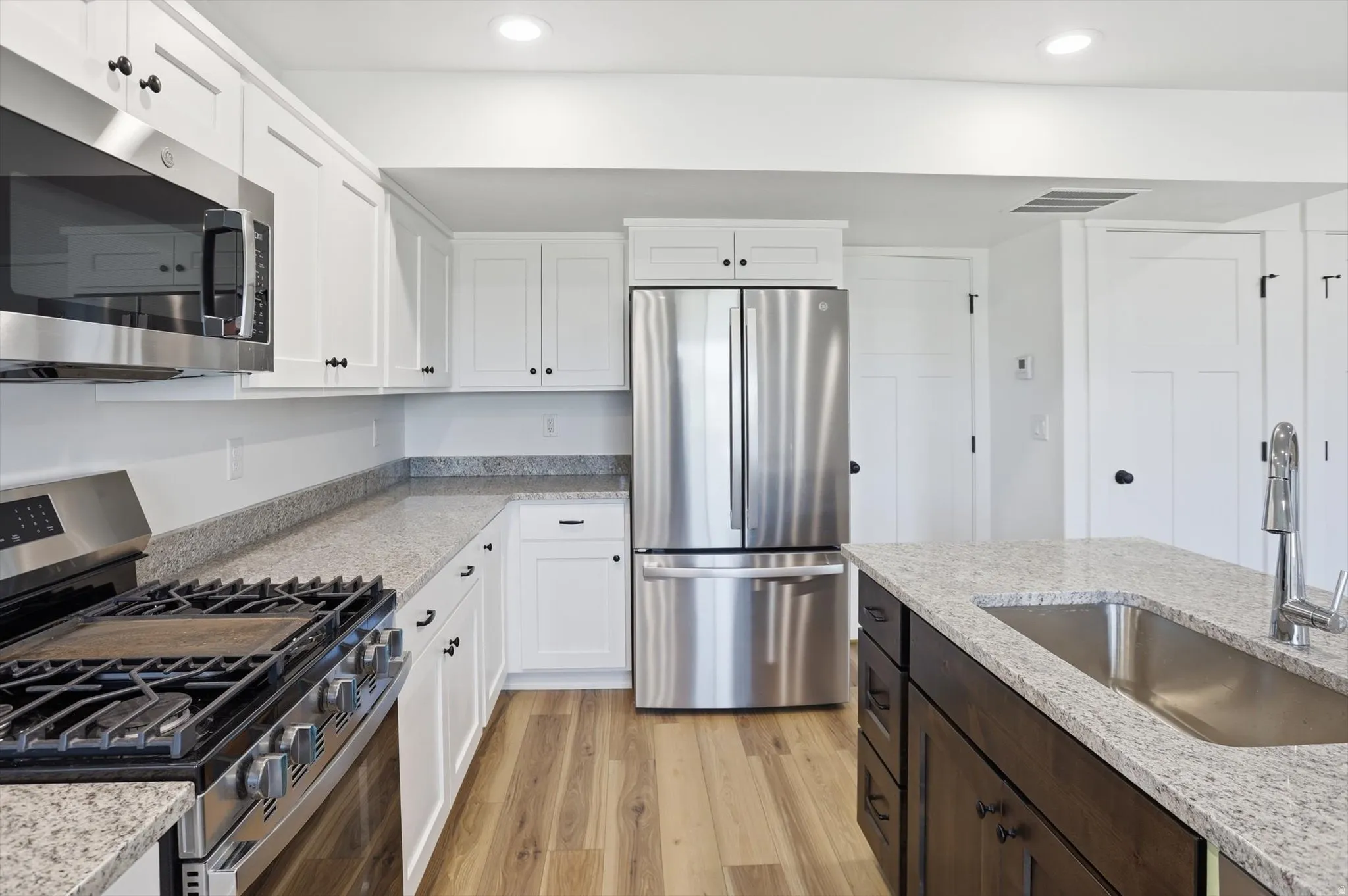 Modern kitchen featuring white shaker cabinetry, stainless steel appliances, speckled countertops, wood-finish flooring, and a central island with an undermount sink