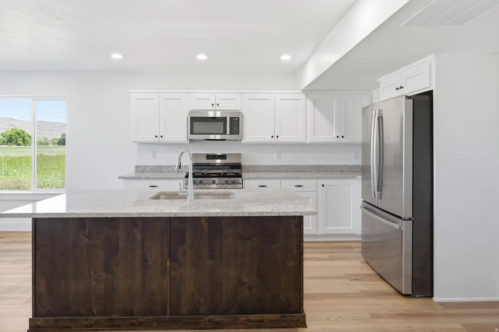 Kitchen featuring a dark wood-finish island with an integrated sink, white perimeter cabinetry, light-toned countertops, and stainless steel appliances