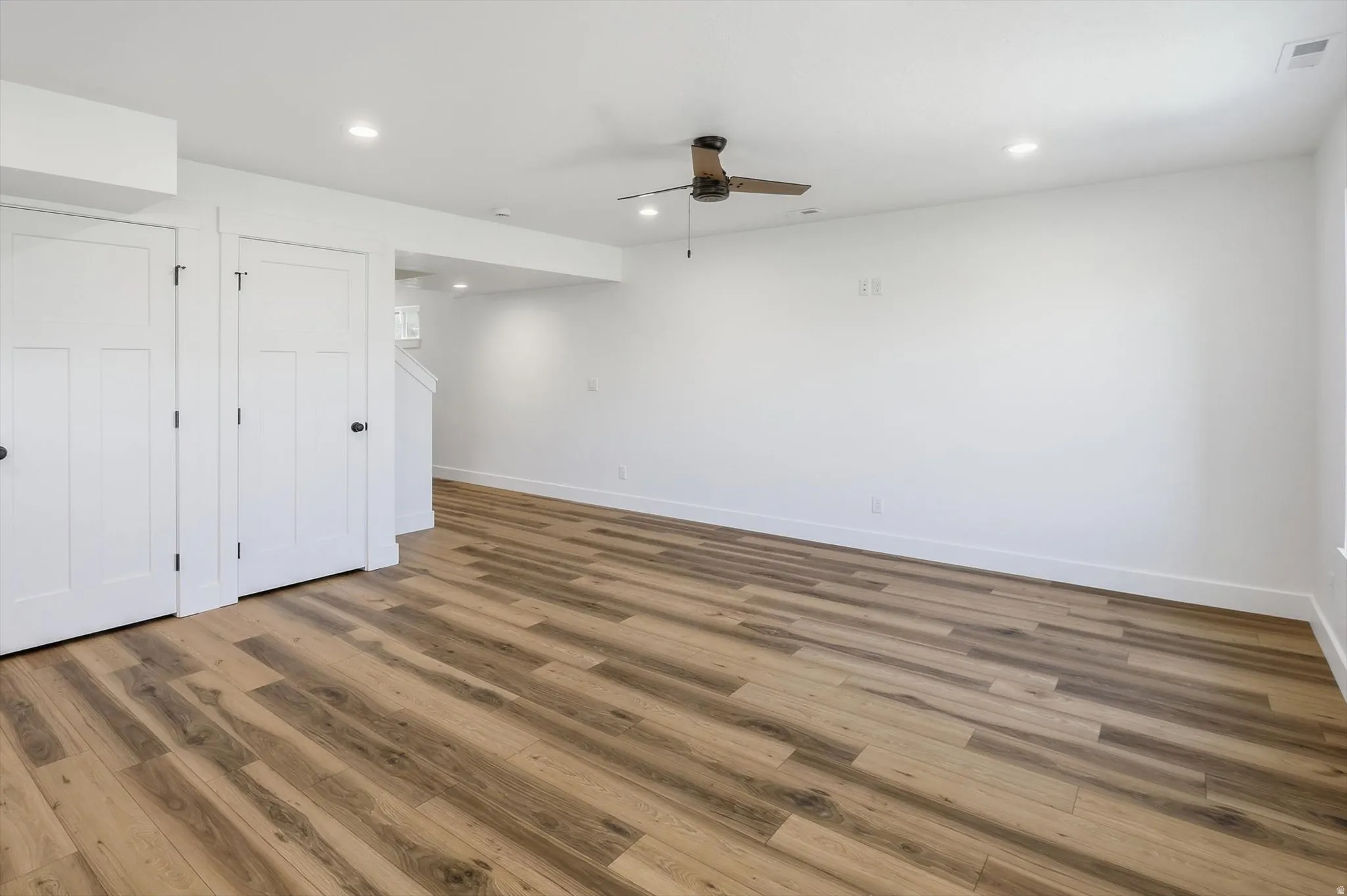 Spacious room featuring wood-finish flooring, white walls, and recessed lighting