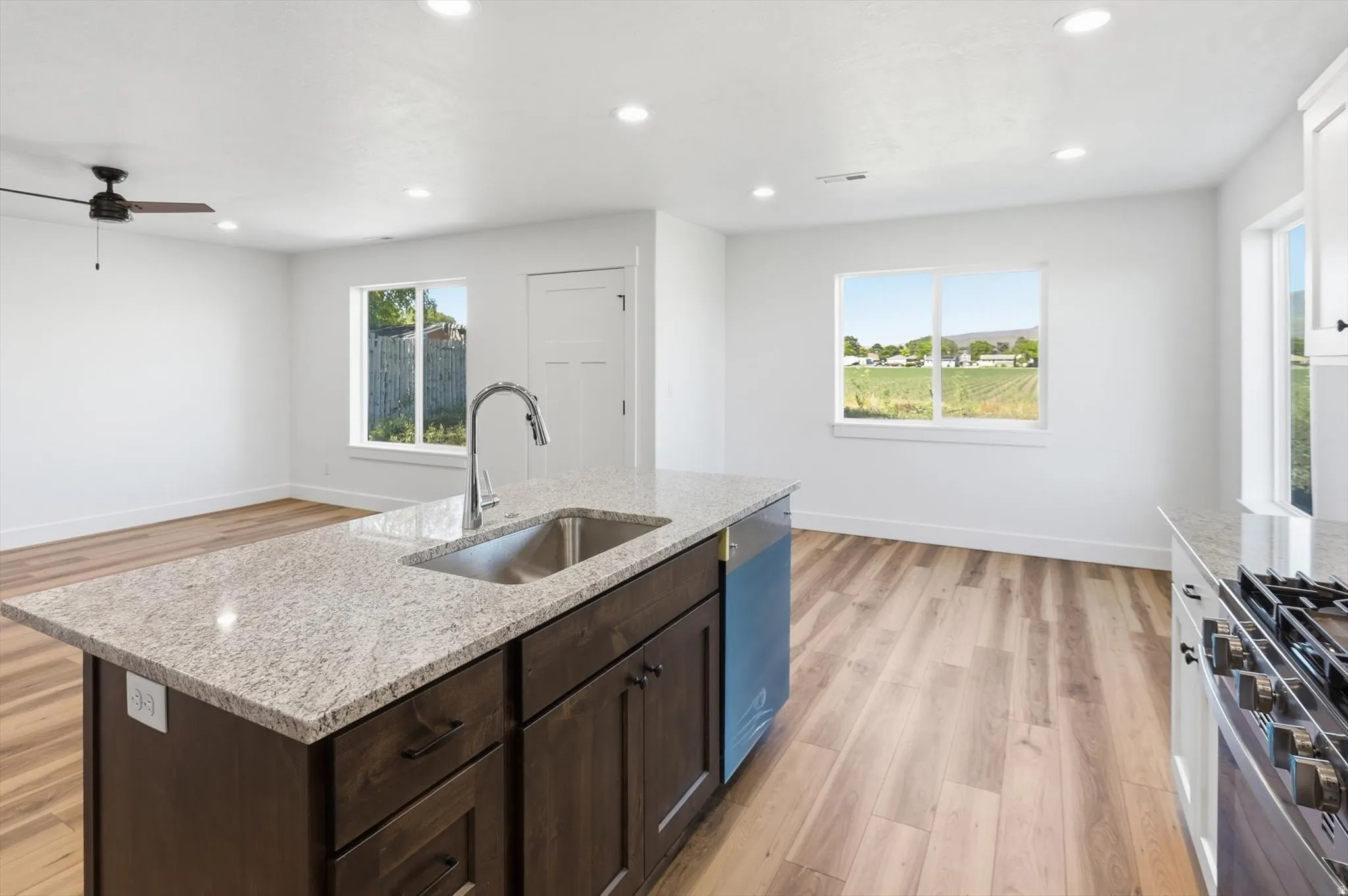 Kitchen island with a stainless steel sink and faucet, integrated dishwasher, dark wood cabinetry, and a light-colored speckled countertop