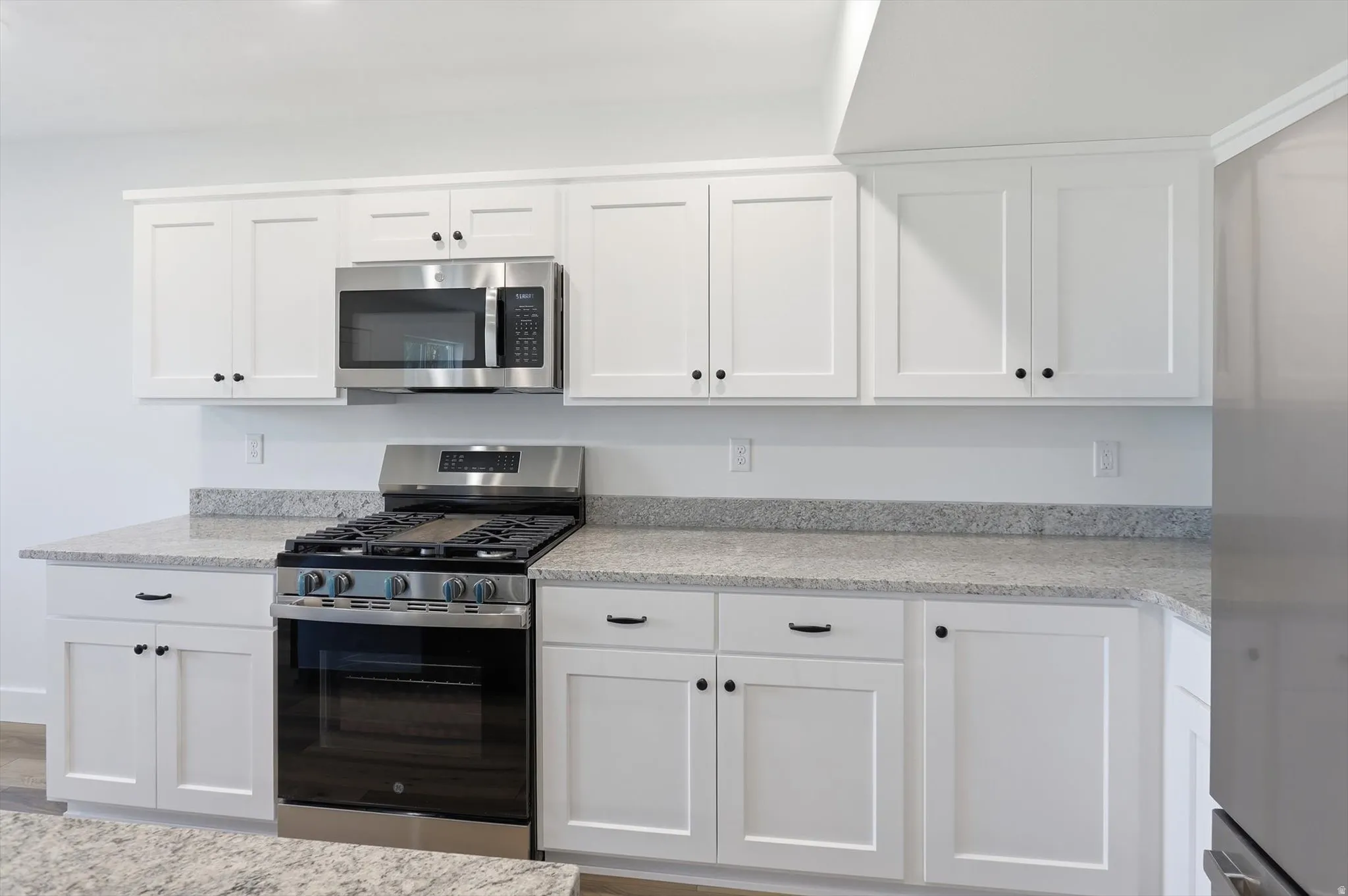 White shaker cabinetry with black hardware, stainless steel gas range, over-the-range microwave, and light-toned speckled countertops