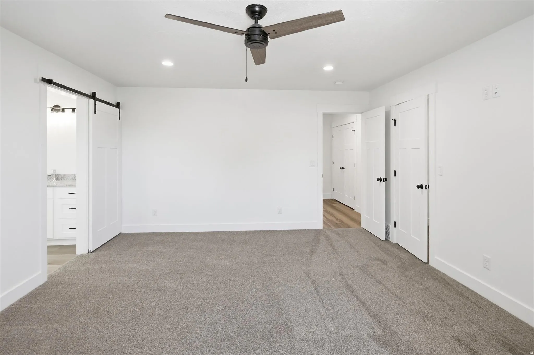 Spacious room featuring neutral carpeting, white walls, and a ceiling fan with integrated lighting