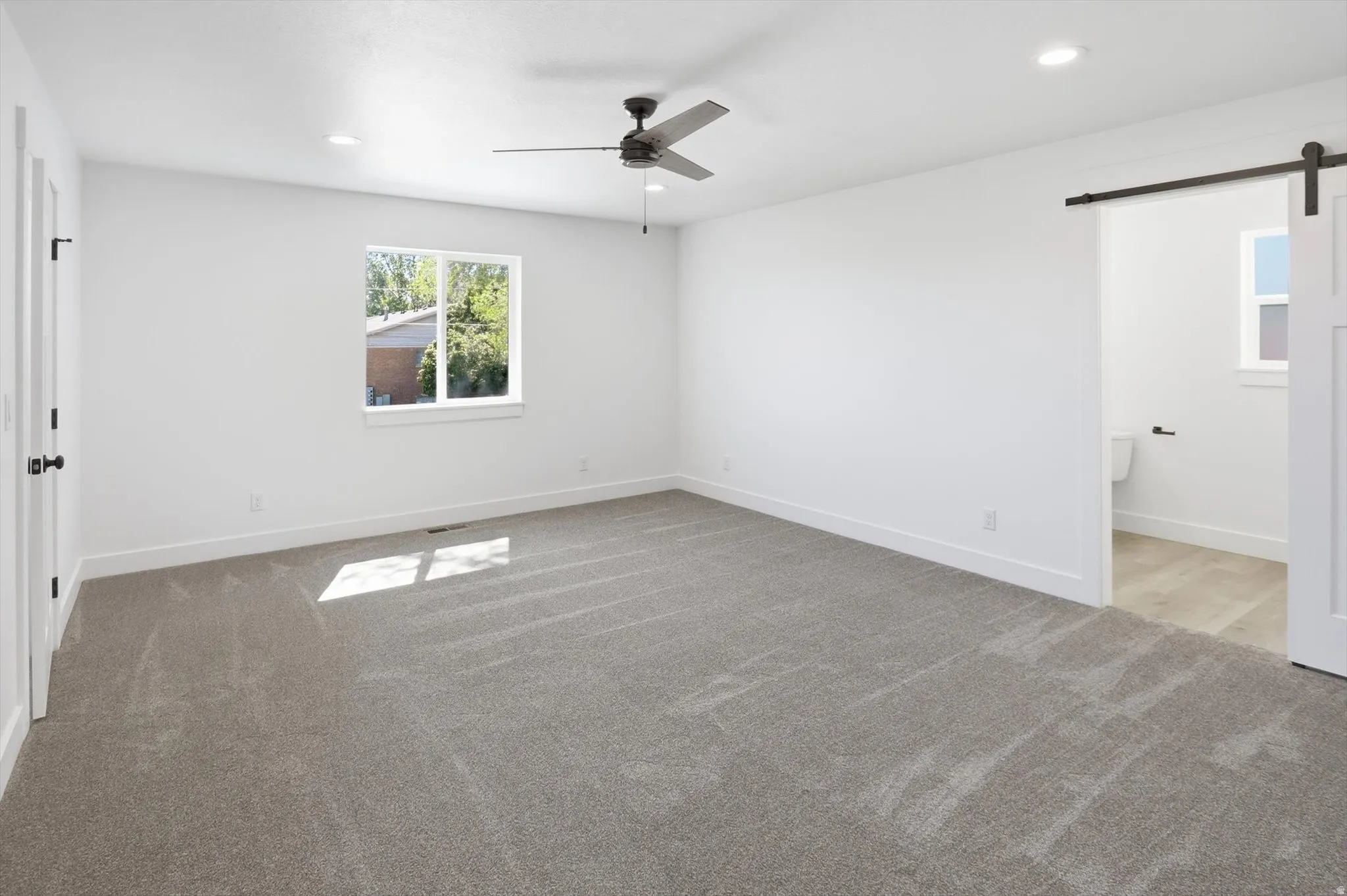 Spacious room featuring neutral carpet, white walls, recessed lighting, and a dark-toned ceiling fan