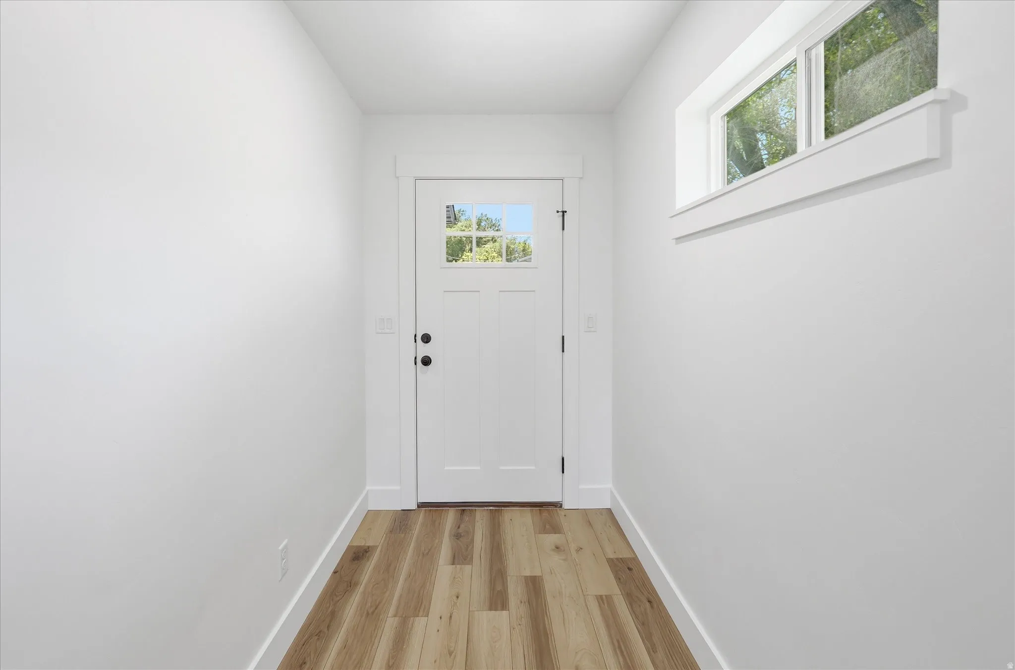 Entryway featuring wood-finish flooring, a white paneled door with glass inserts, and a high horizontal window