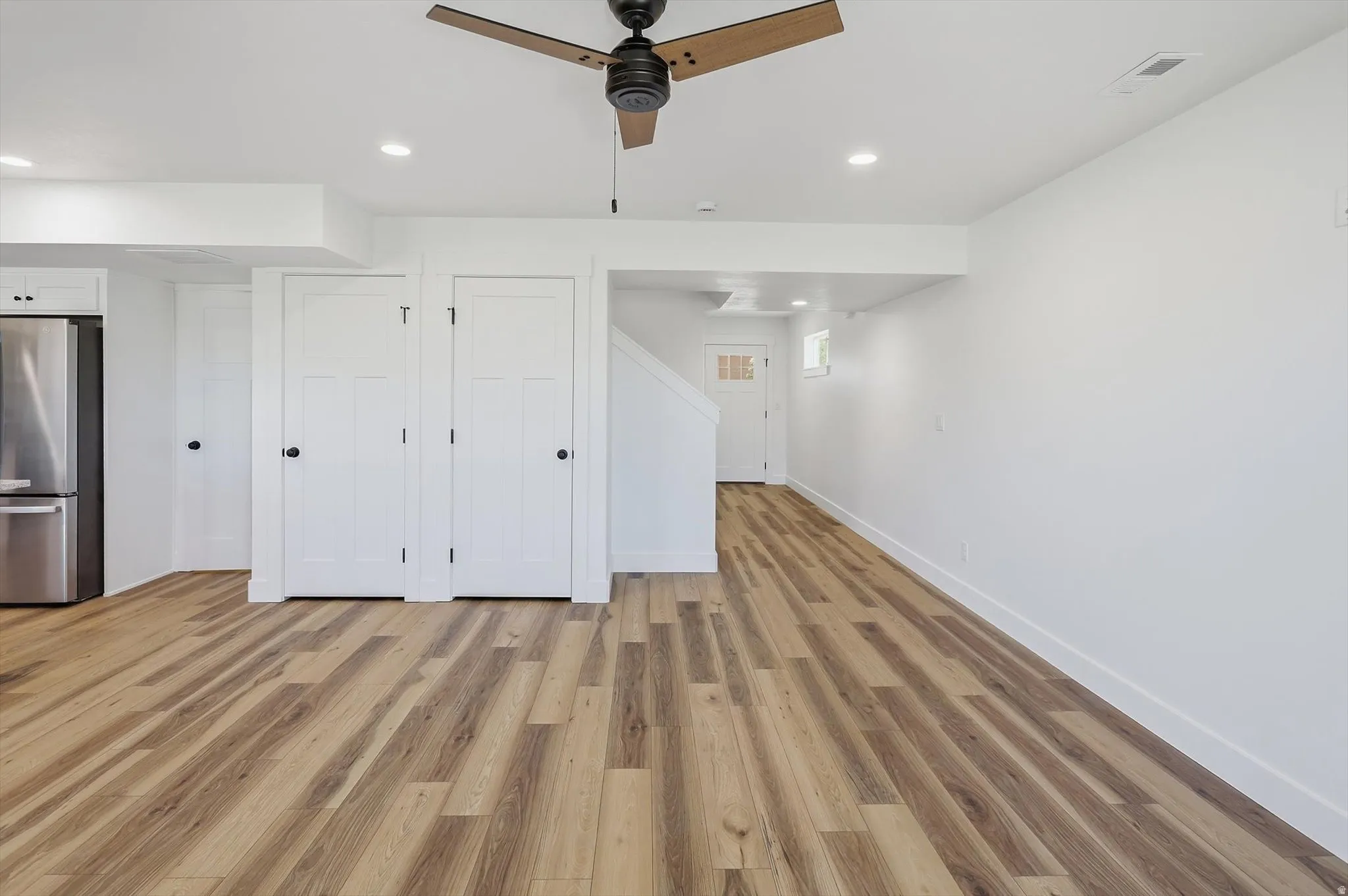 Spacious open-concept area featuring wood-finish flooring, recessed ceiling lighting, and a prominent ceiling fan with wood-look blades
