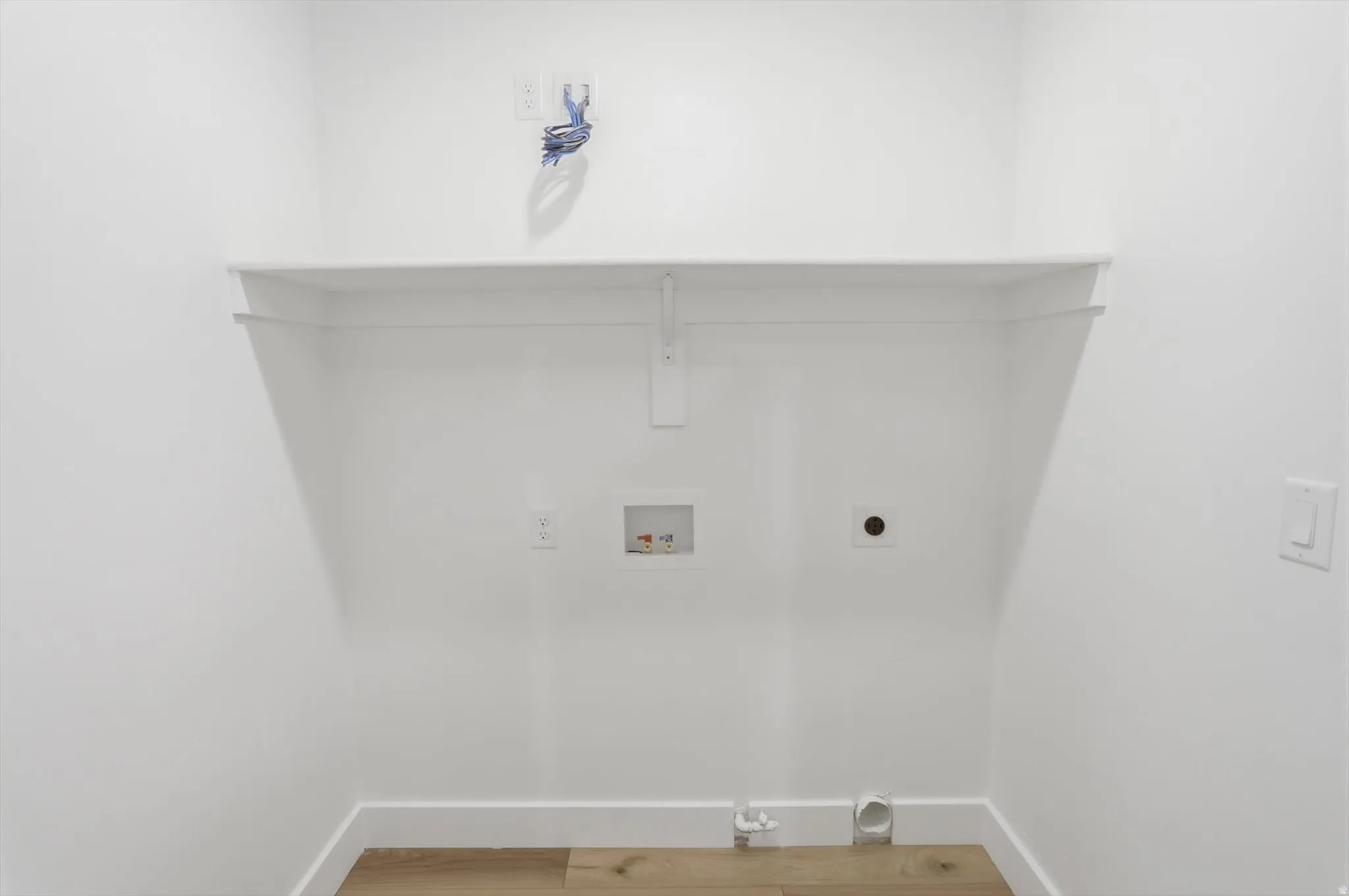 Dedicated laundry area featuring a white wall shelf, utility hookups, and wood-finish flooring