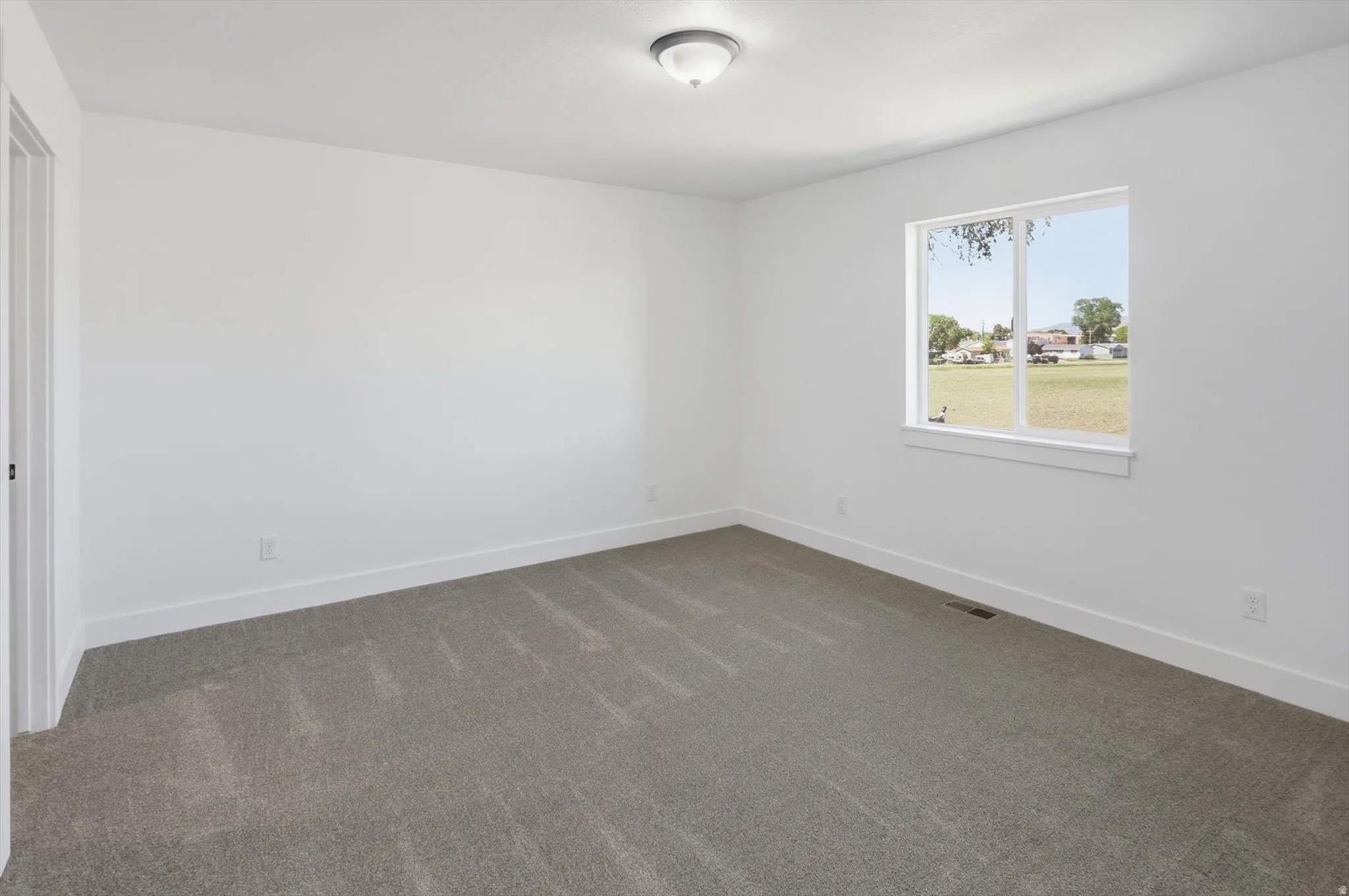 Spacious room featuring neutral carpeting, white walls, and a large window providing natural illumination