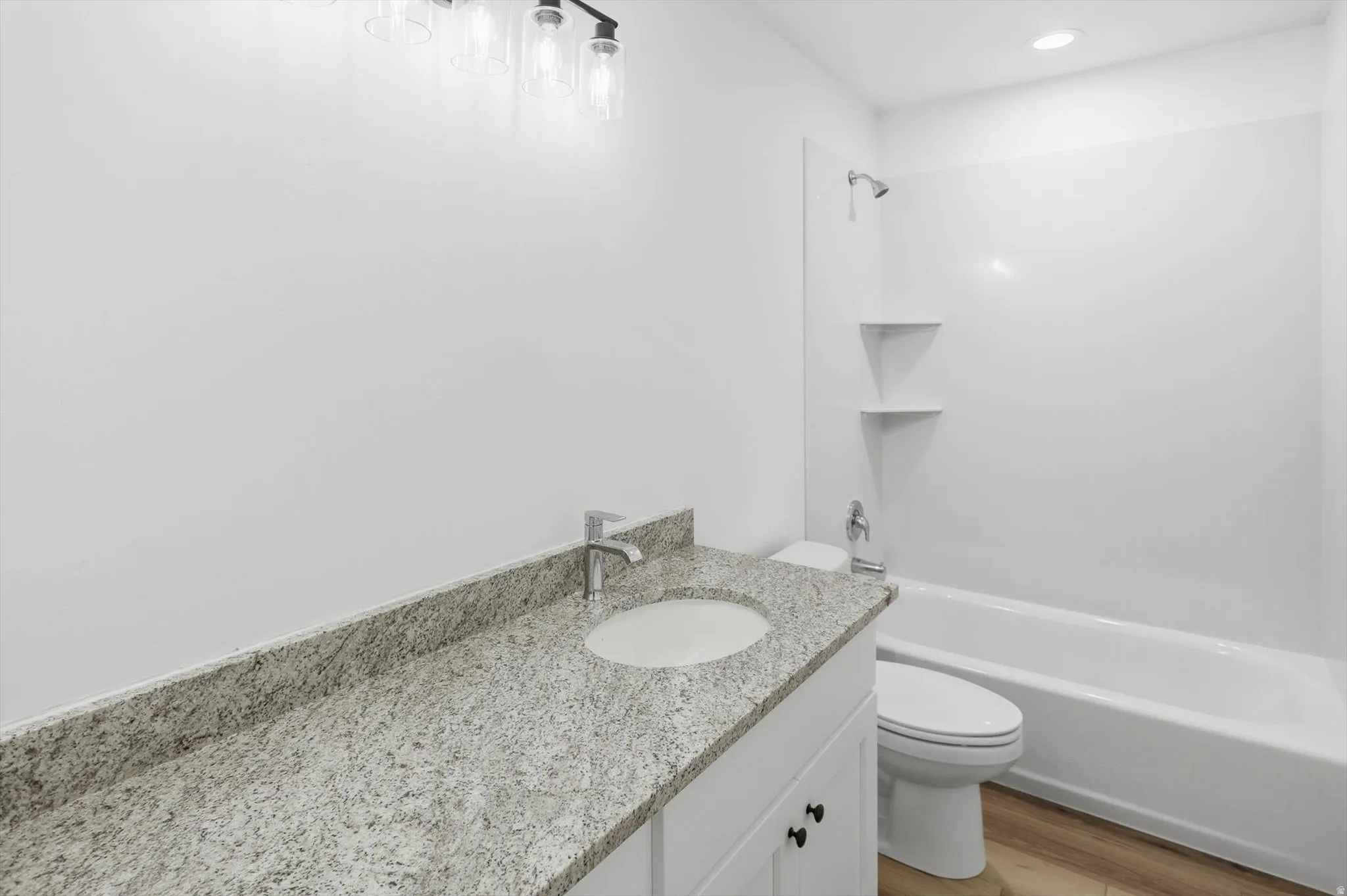 Bathroom featuring a granite-finish vanity, undermount sink, and a white shower/tub combination with integrated shelving