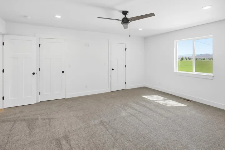 Spacious room featuring neutral carpeting, white walls, a ceiling fan, and a large window with a scenic landscape