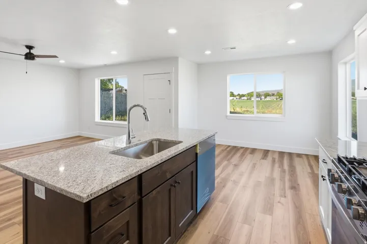 Kitchen island with a stainless steel sink and faucet, integrated dishwasher, dark wood cabinetry, and a light-colored speckled countertop