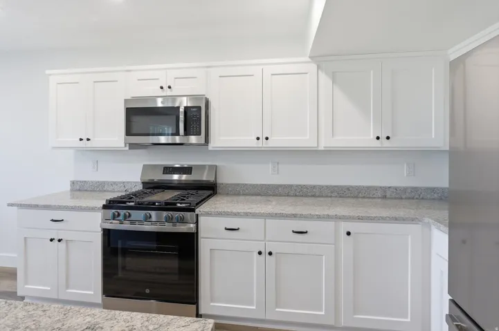 White shaker cabinetry with black hardware, stainless steel gas range, over-the-range microwave, and light-toned speckled countertops
