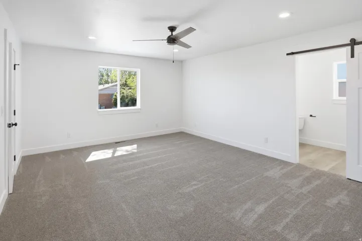 Spacious room featuring neutral carpet, white walls, recessed lighting, and a dark-toned ceiling fan
