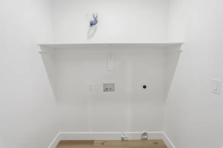 Dedicated laundry area featuring a white wall shelf, utility hookups, and wood-finish flooring