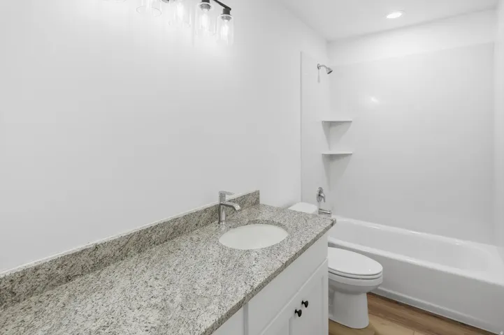 Bathroom featuring a granite-finish vanity, undermount sink, and a white shower/tub combination with integrated shelving