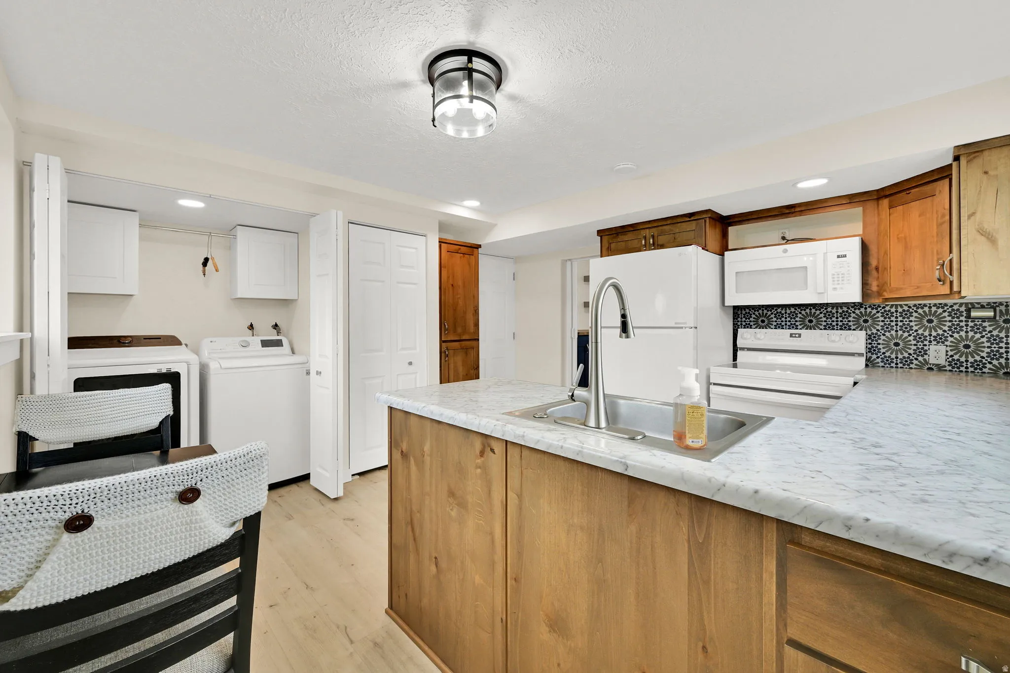 Kitchen featuring wood-finish cabinetry, patterned tile backsplash, and light-toned countertops