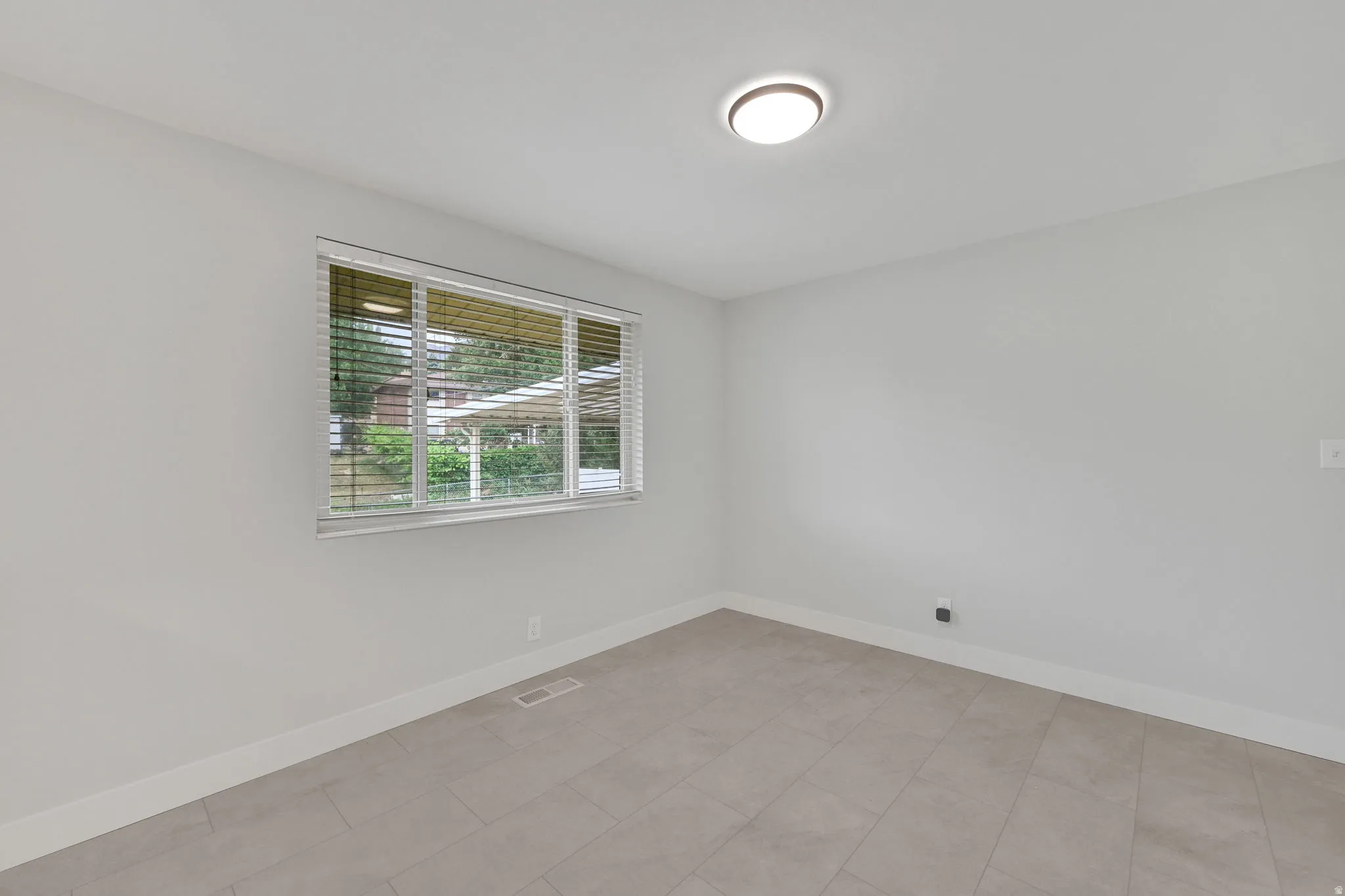 Neutral tone wall paint, contemporary flush-mount ceiling light, white baseboards, and window with horizontal blinds