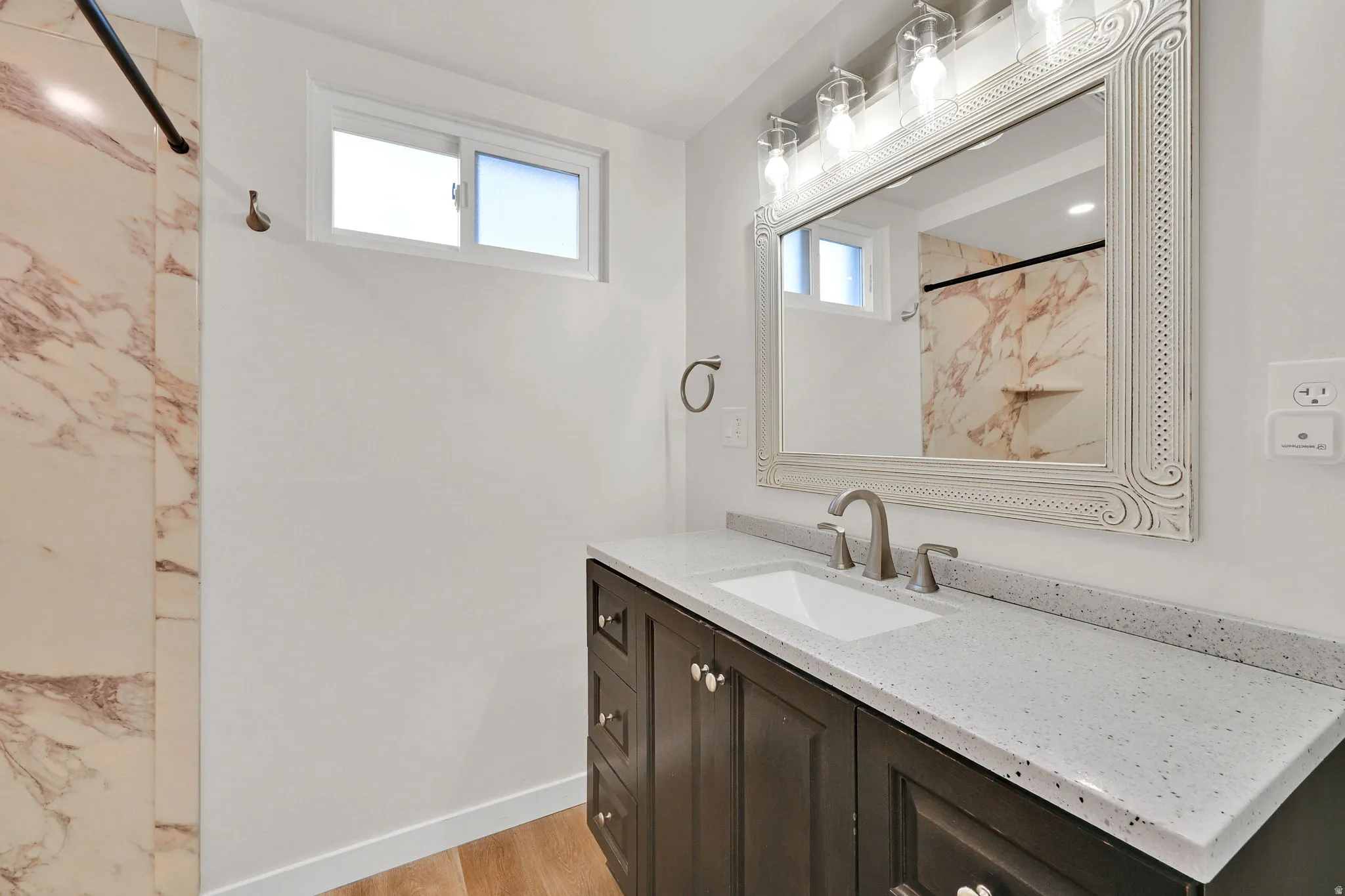 Bathroom featuring a dark wood vanity with a light speckled countertop, an undermount sink, and a framed mirror