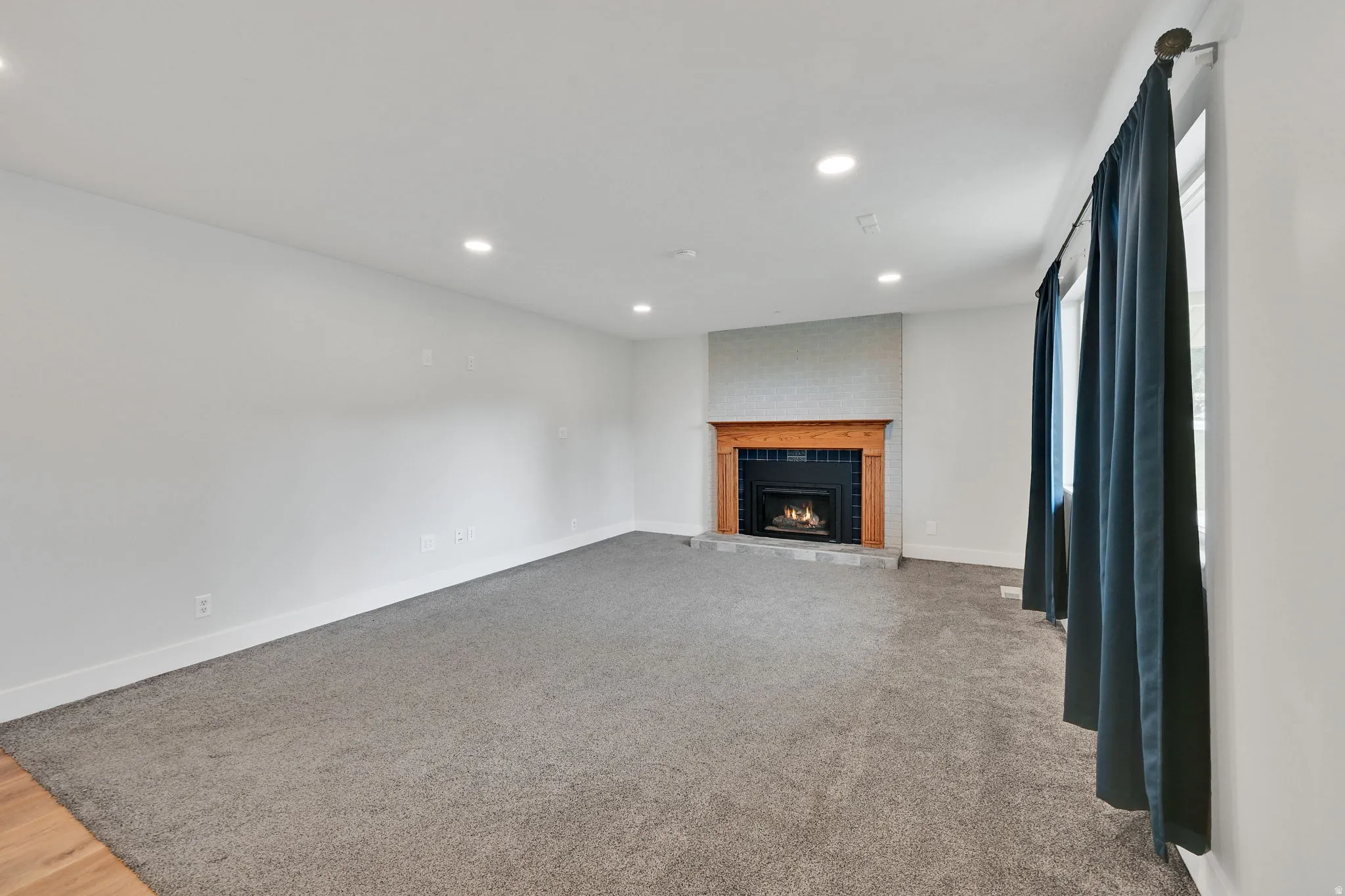 Living space featuring a fireplace with a wood mantle and stone surround, recessed lighting, gray carpeting, and white baseboards