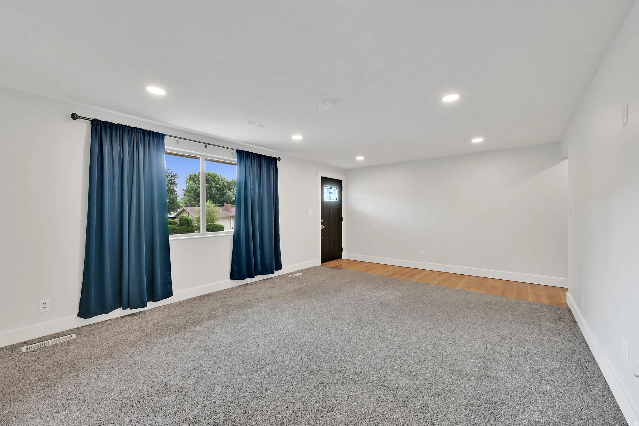 Spacious room featuring gray carpet, white walls, recessed lighting, and a window with white trim