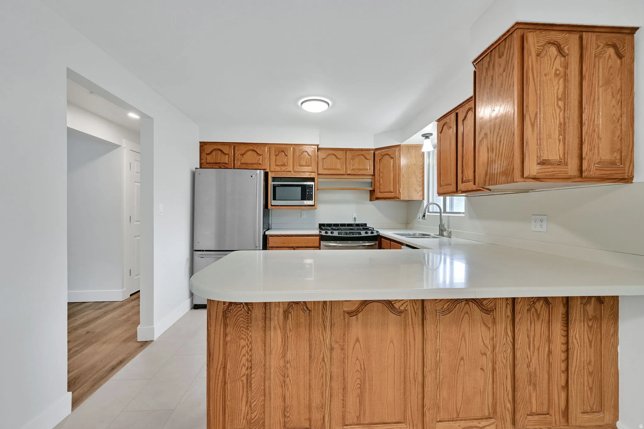 Kitchen featuring wood cabinetry, light-toned countertops, stainless steel appliances, and tile flooring