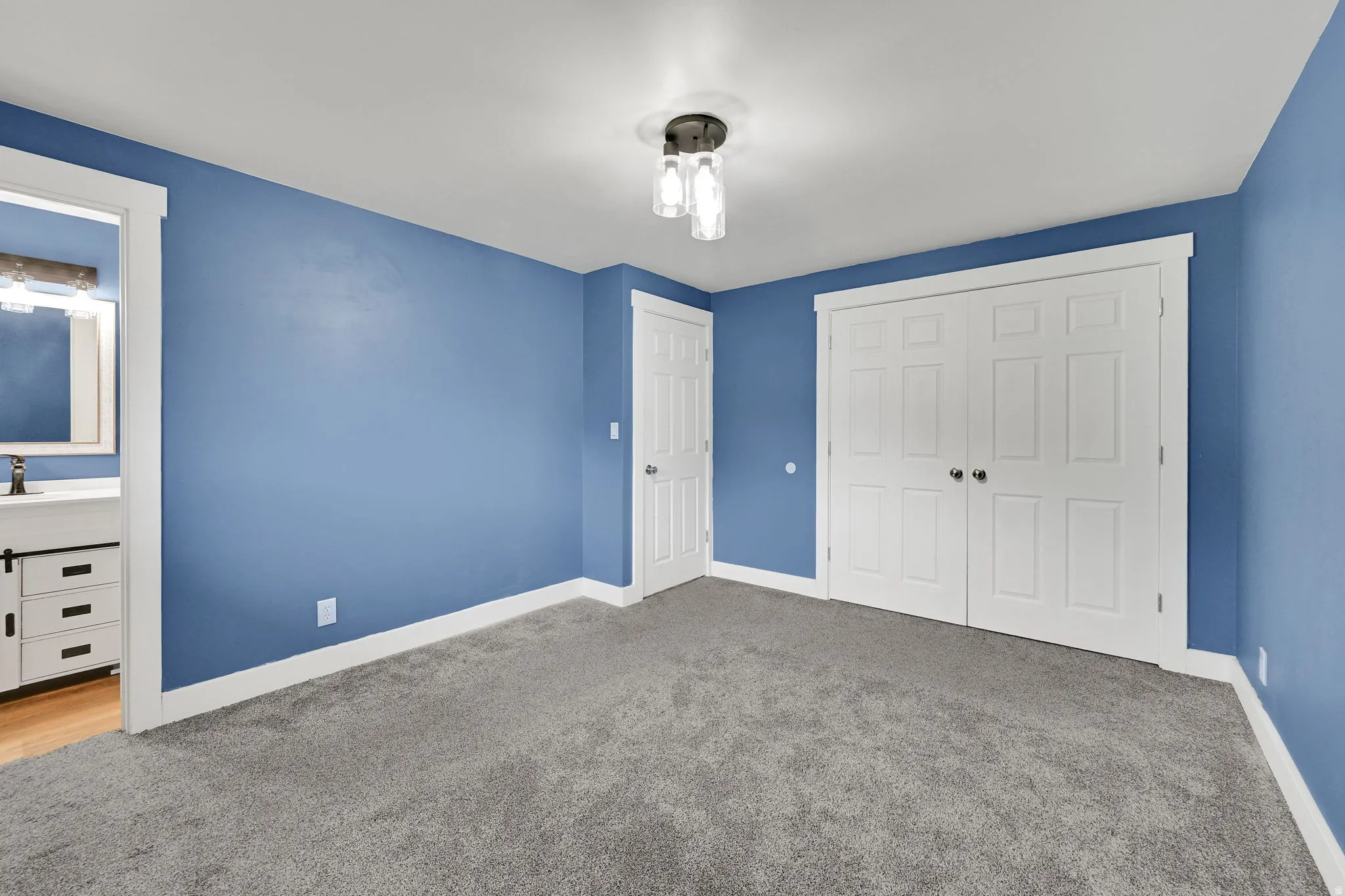 Spacious room featuring plush gray carpeting, white baseboards, a white six-panel bifold closet, and a contemporary ceiling light fixture