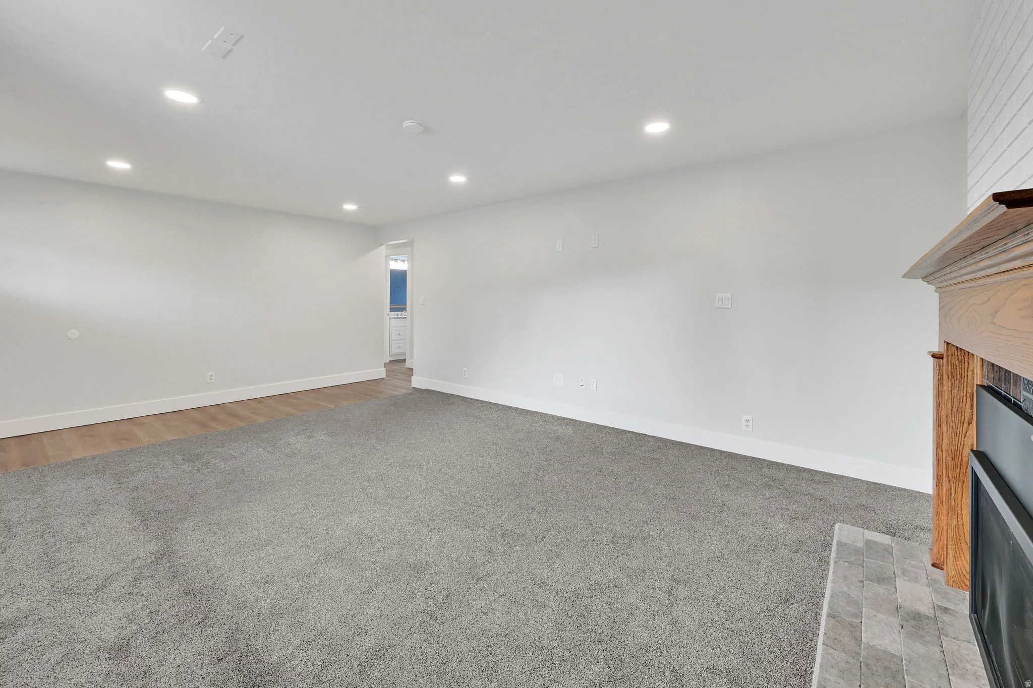 Spacious living area featuring neutral carpeting, recessed lighting, wood-finish flooring, a fireplace with a wood mantle, and a tile hearth