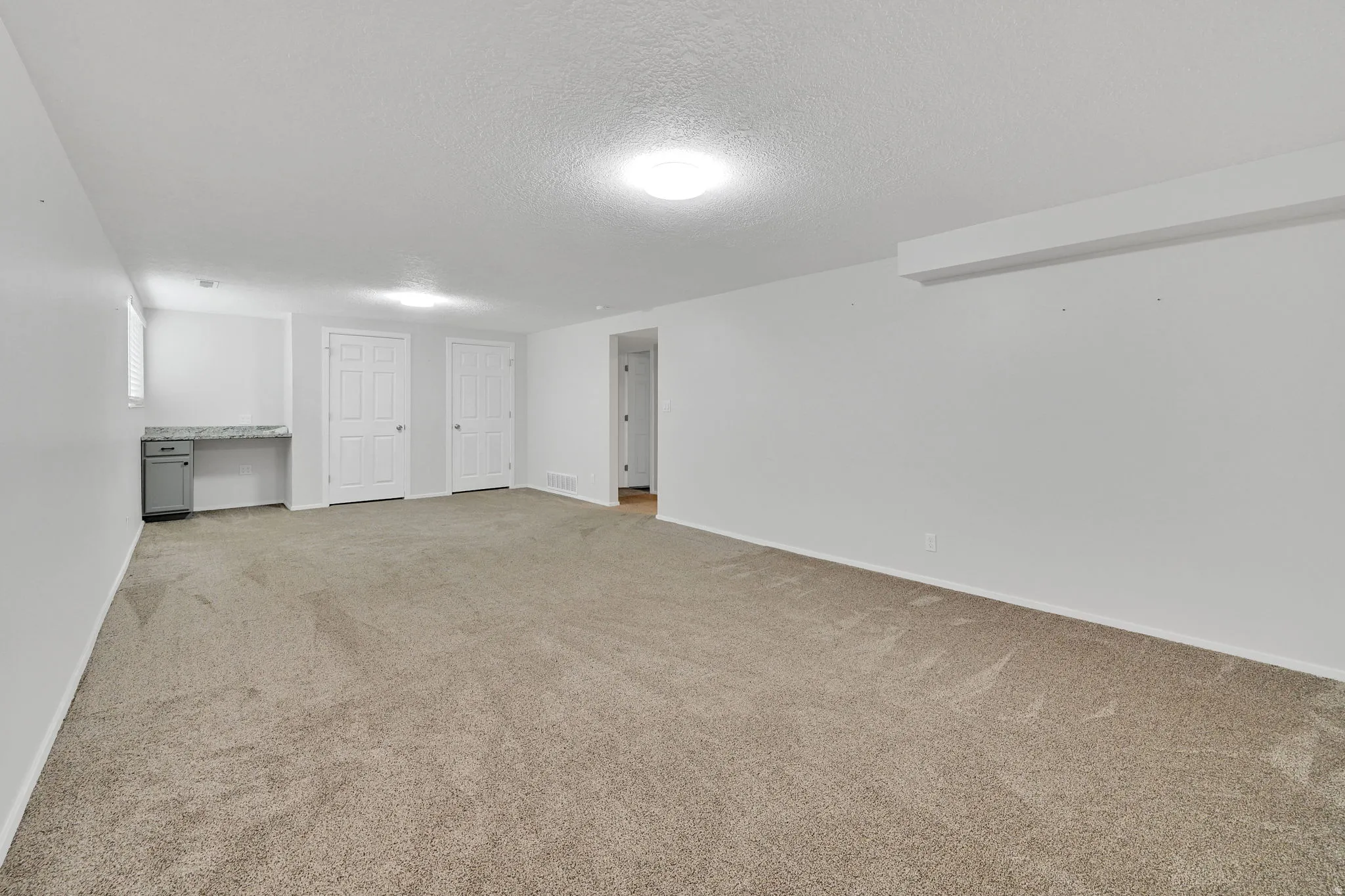 Spacious carpeted room featuring a built-in desk with a light-colored countertop, two panel doors, and recessed lighting