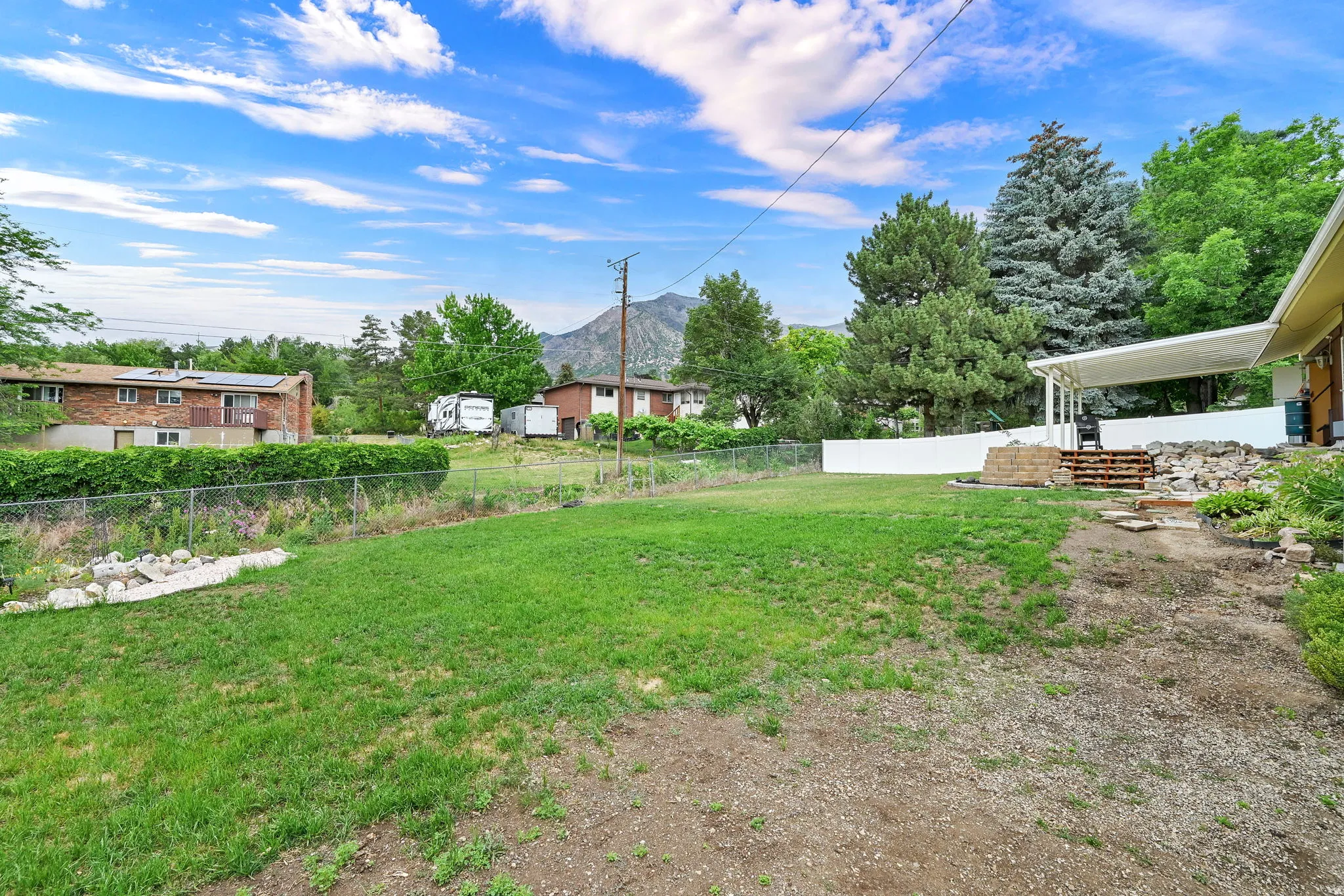 Expansive grassy area with mature trees and a white privacy fence