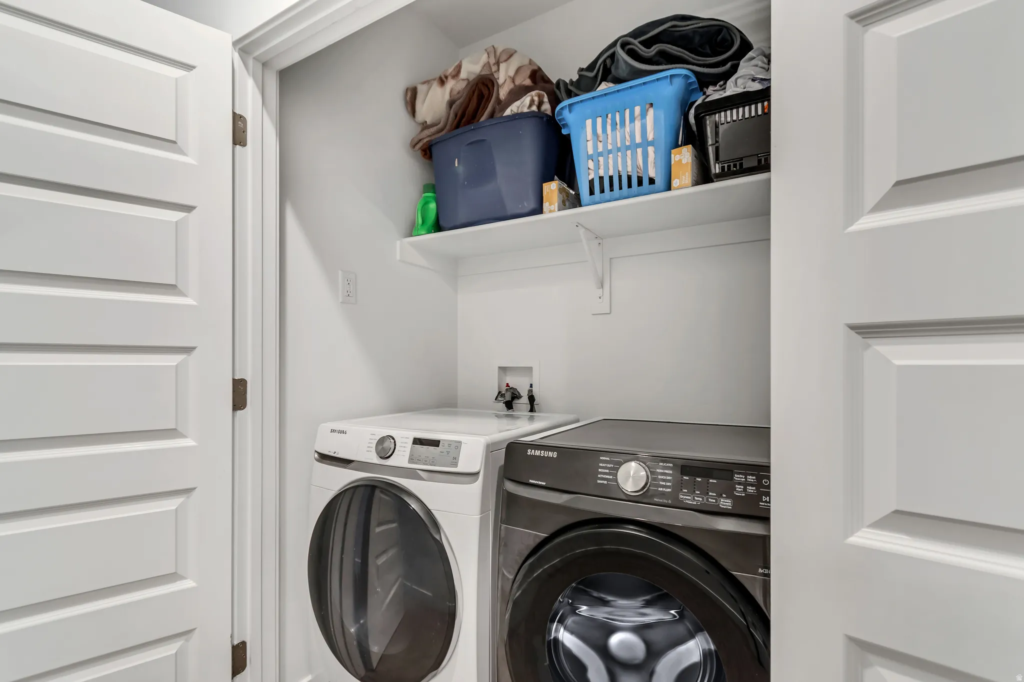 Dedicated laundry closet featuring a built-in shelf for storage, white paneled doors, and white walls