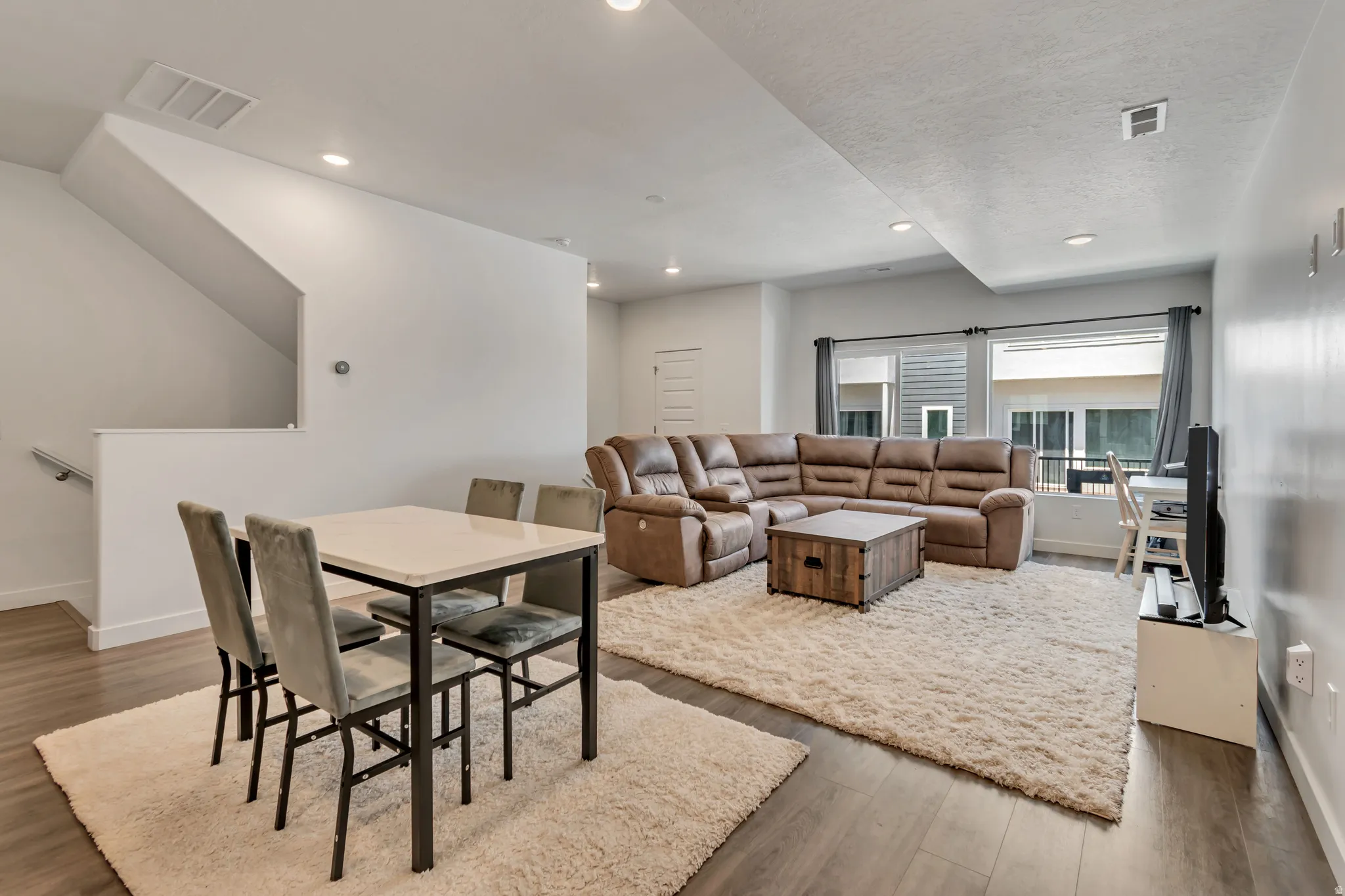 Open-concept living area featuring wood-finish flooring, recessed lighting, and a prominent staircase with a modern handrail