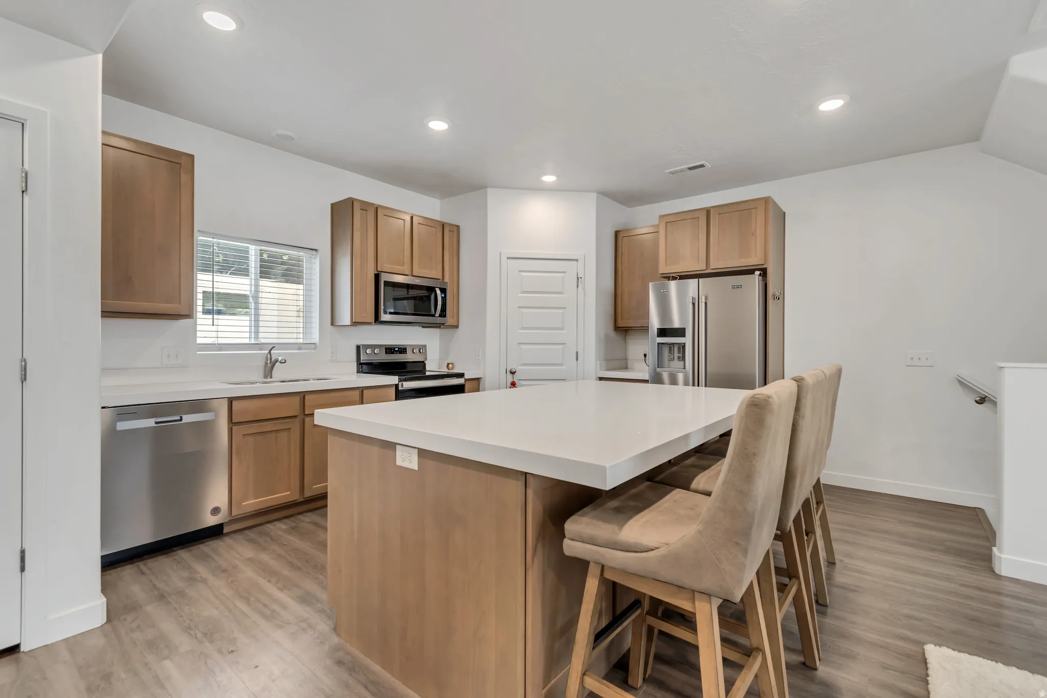 Kitchen featuring a central island with countertop seating, stainless steel appliances, wood-finish cabinetry, light-toned countertops, and recessed lighting