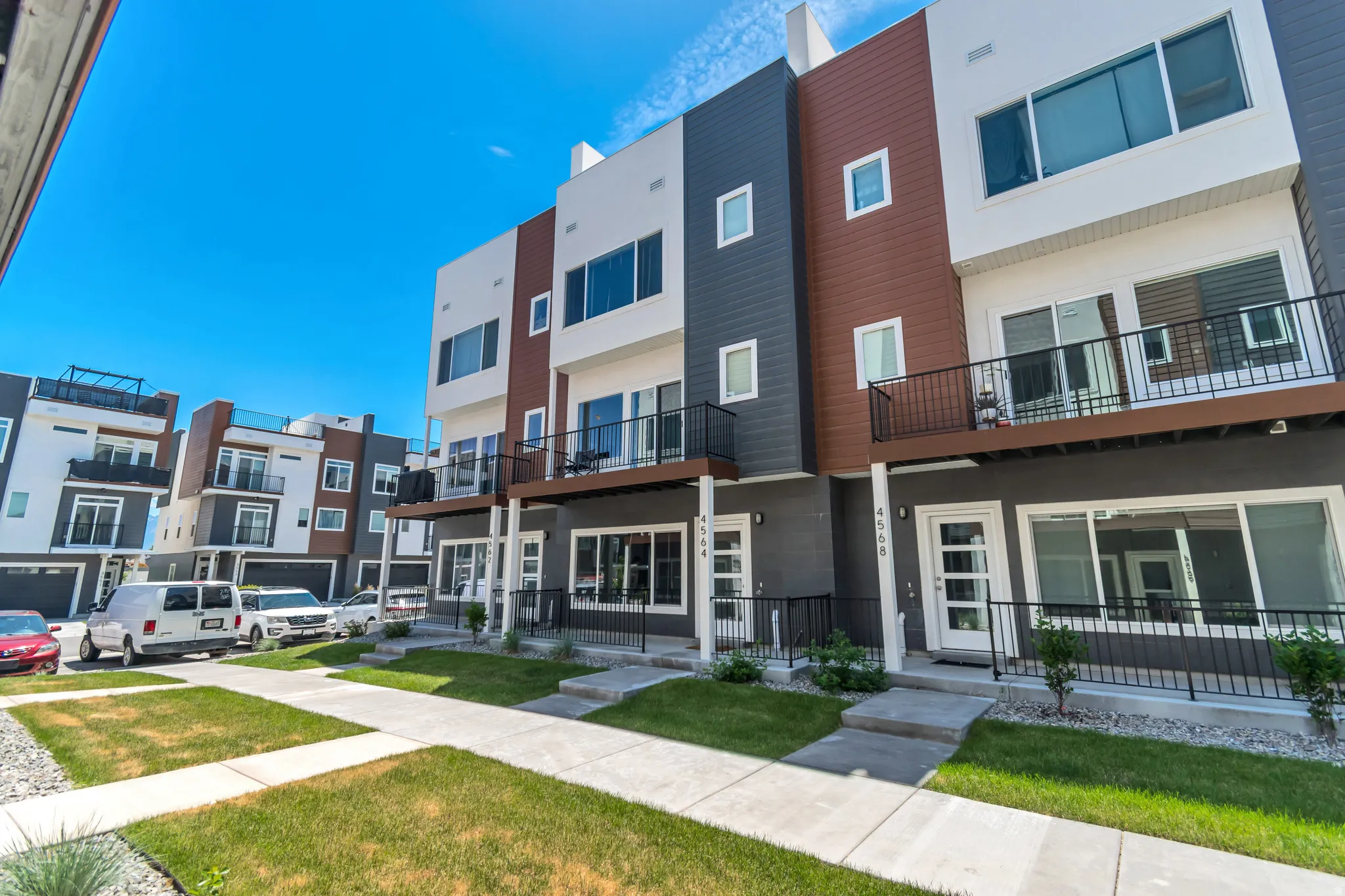 Modern townhome exterior featuring multi-toned siding, a private balcony with black railings, and a ground-level patio