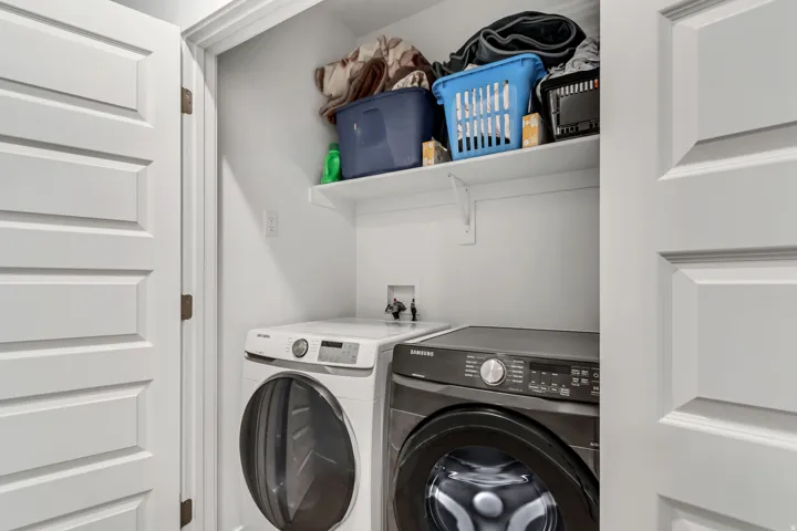 Dedicated laundry closet featuring a built-in shelf for storage, white paneled doors, and white walls