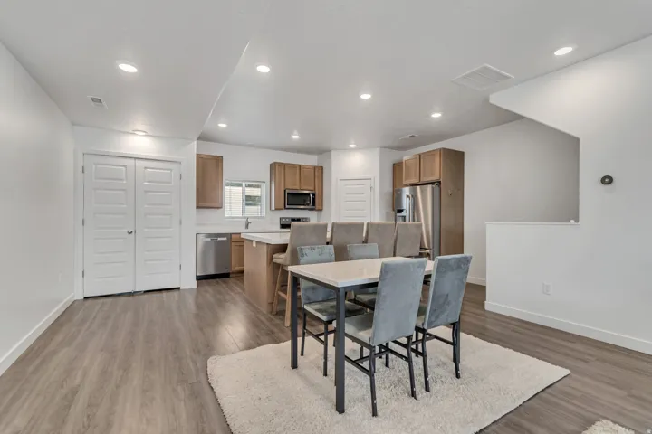 Open-concept living area featuring wood-finish flooring, recessed lighting, and a kitchen with light wood cabinetry and stainless steel appliances