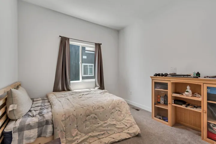 Neutral-toned bedroom featuring a large window with privacy coverings, light gray walls, and plush carpeting
