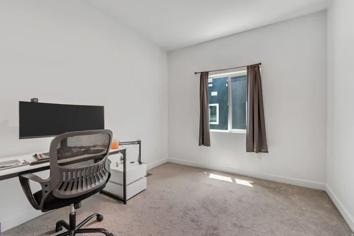 Carpeted room with a double-pane window featuring dark drapes, white walls, and white baseboards