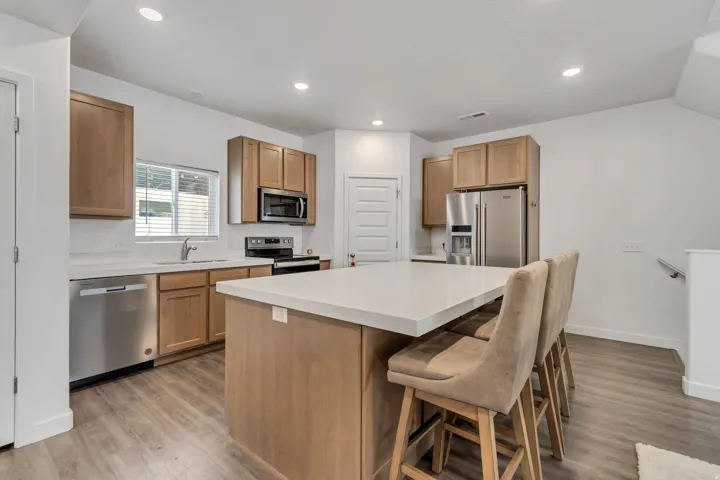 Kitchen featuring a central island with countertop seating, stainless steel appliances, wood-finish cabinetry, light-toned countertops, and recessed lighting