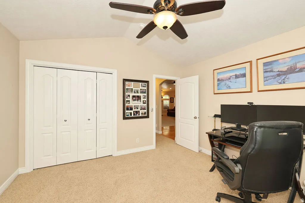 Neutral-toned room with vaulted ceiling and a ceiling fan with integrated lighting