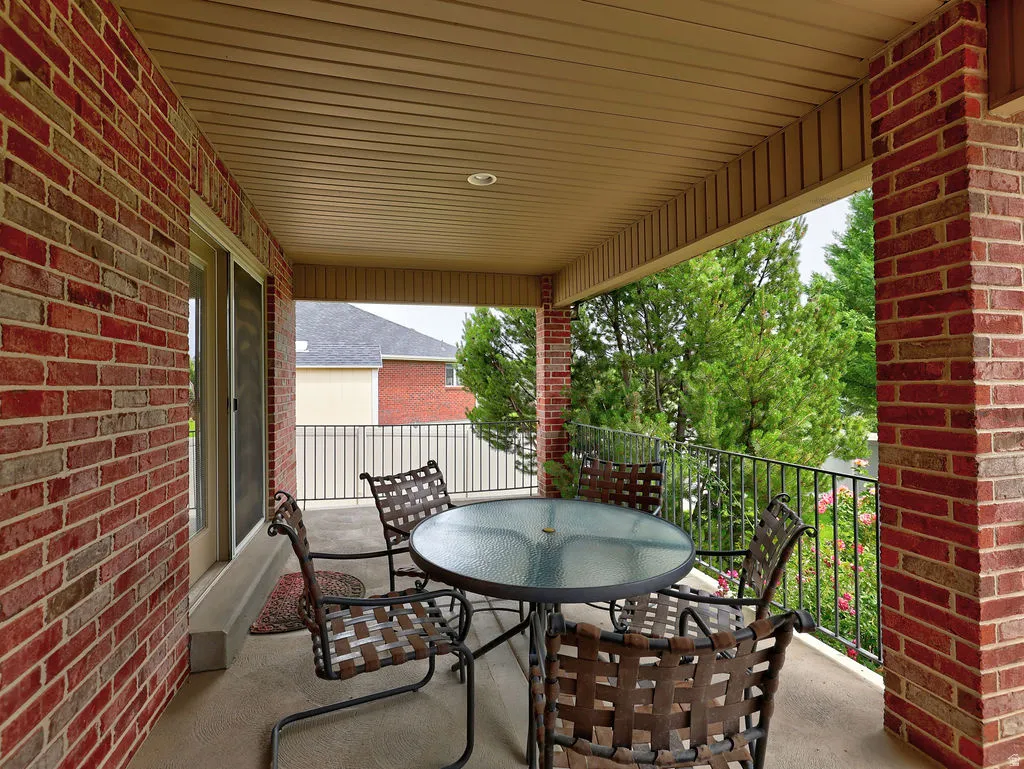 Covered concrete patio featuring a brick exterior wall, a tan plank ceiling, and a black wrought iron railing