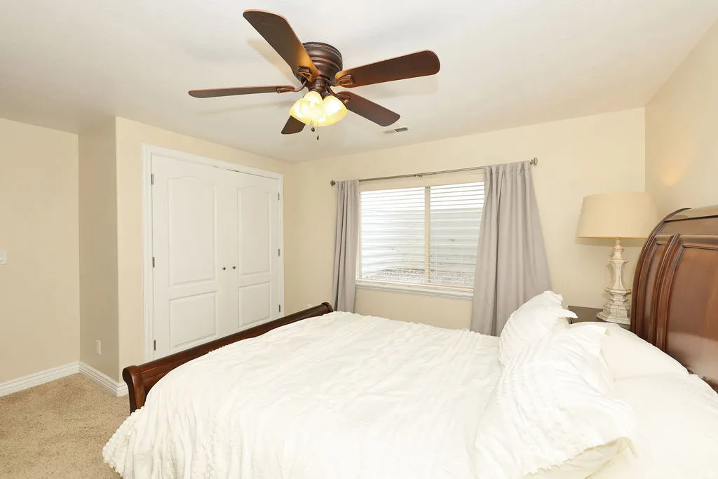 Recessed window with horizontal blinds, double-door closet with white paneling, ceiling-mounted fan with integrated lighting, light-toned carpeting, and a neutral wall color