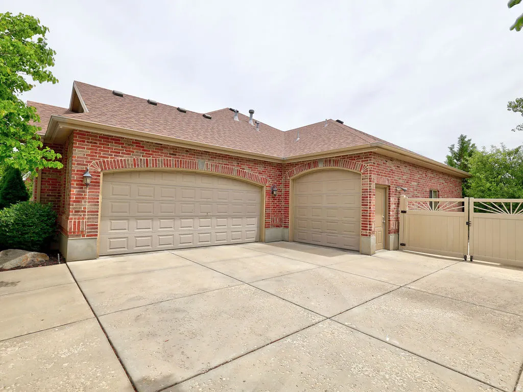 Brick exterior featuring two arched garage doors, a concrete driveway, and a decorative privacy gate
