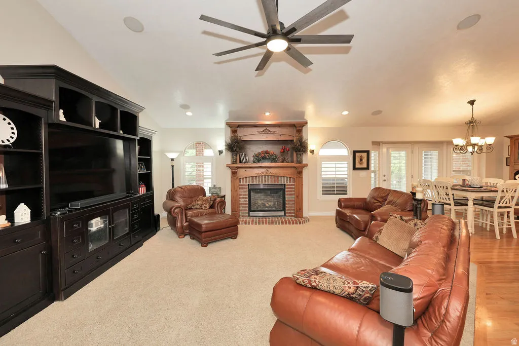 Living area featuring vaulted ceilings, a built-in media center with dark wood-finish cabinetry, a brick fireplace with a wood mantel, and arched windows with plantation shutters
