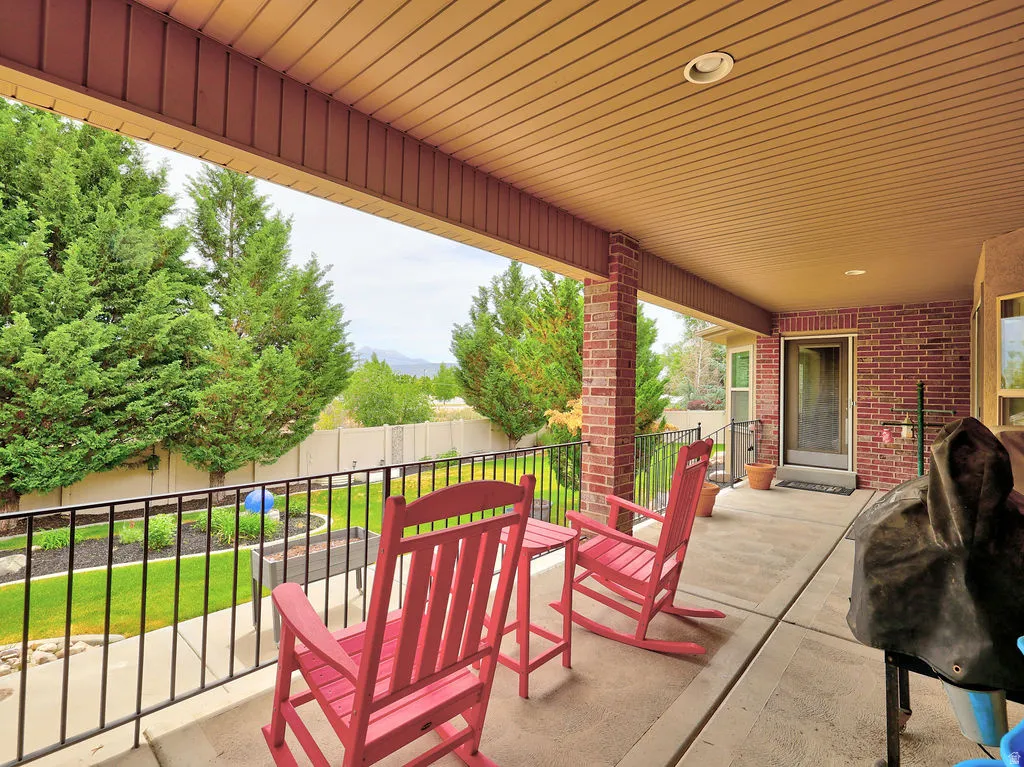 Covered patio with a planked ceiling and recessed lighting, featuring brick pillars and a black metal railing