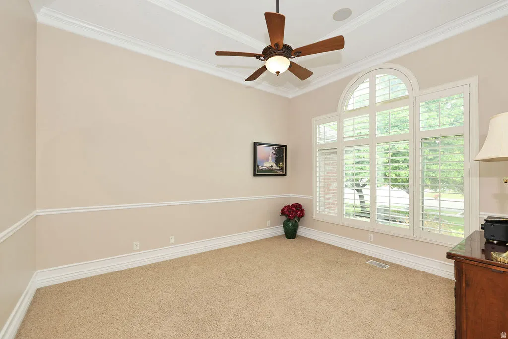 Arched window with plantation shutters, crown molding, chair rail molding, ceiling fan, and recessed ceiling speaker
