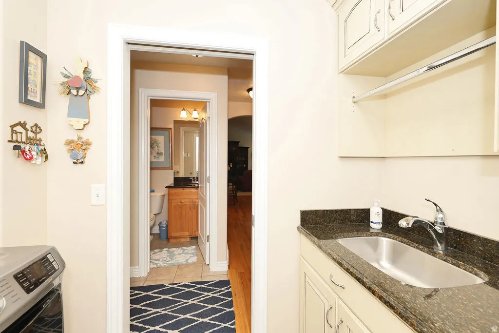 Utility sink with a dark speckled countertop, cream cabinetry, and an upper storage shelf with a hanging rod