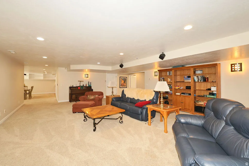 Spacious lower-level living area with recessed lighting, plush carpeting, built-in wood shelving, and sconce lighting