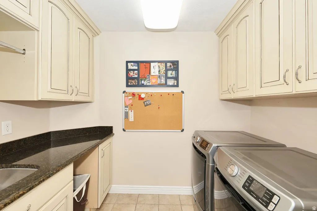 Utility room featuring extensive upper cabinetry, a built-in sink with dark countertop, tile flooring, and integrated laundry rod