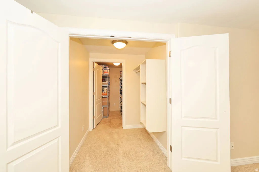 Double panel doors opening to a carpeted hallway with built-in shelving, leading to an additional room with tile flooring and interior lighting