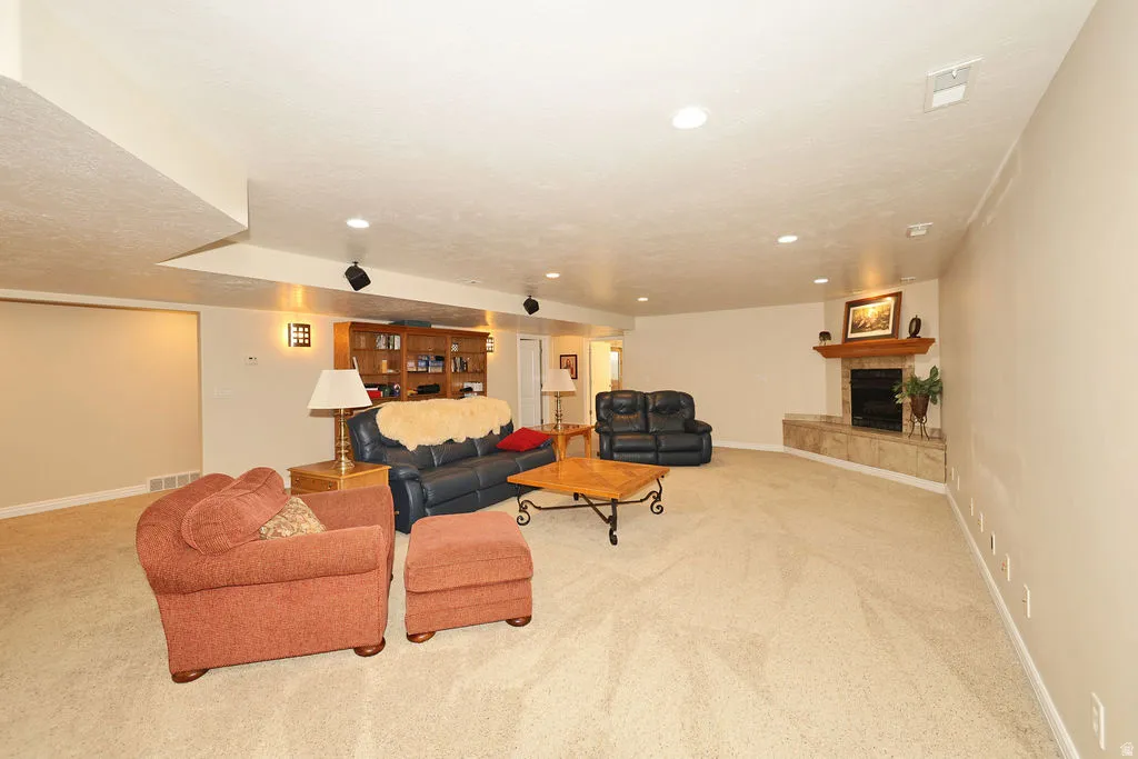 Spacious entertainment area featuring recessed lighting, a built-in wood-finish bookshelf, and a corner fireplace with a stone surround and wood mantle